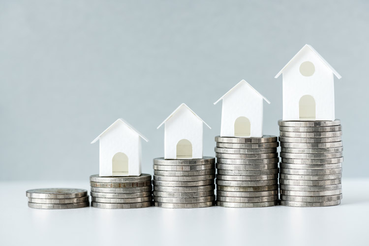 Four paper houses on top of stacks of quarters